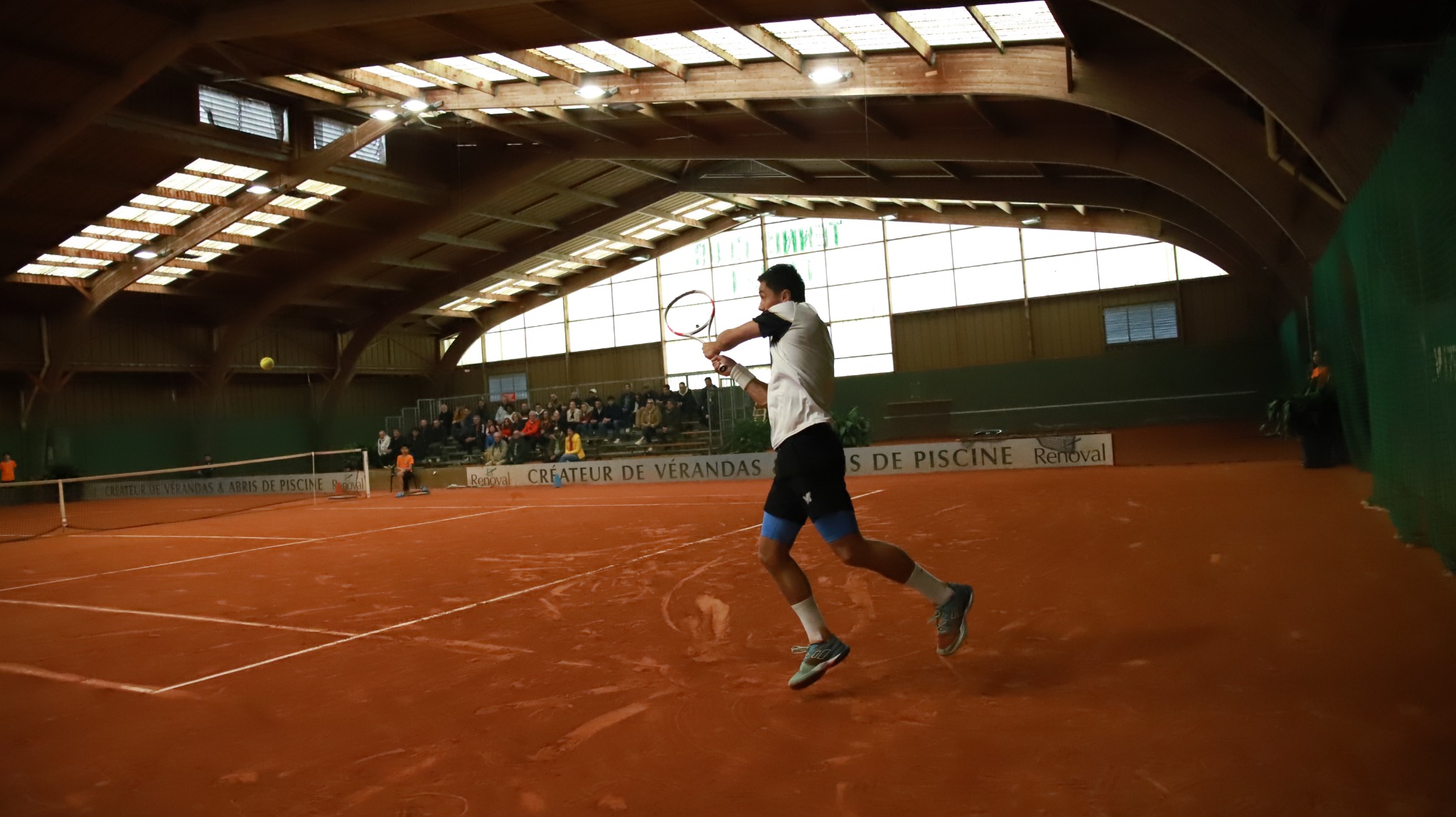 Joueur exécutant un revers devant le public lors d’une compétition au Tennis Club Cholet